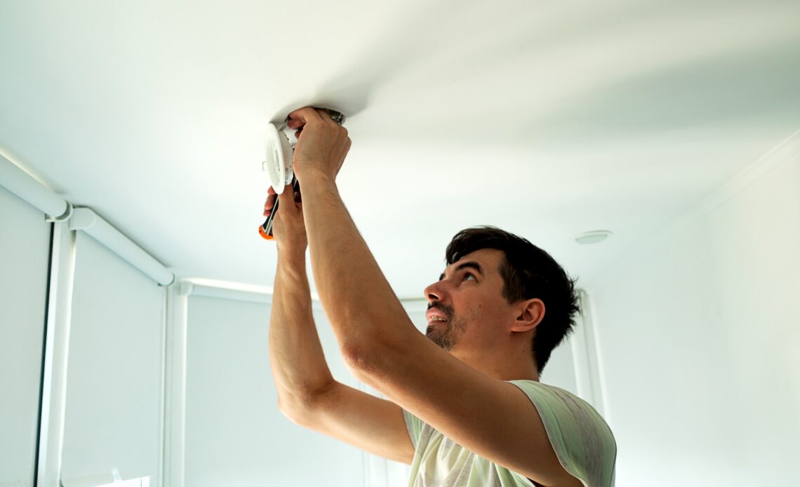 House master male electrician repairs ceiling light indoor home in white room.