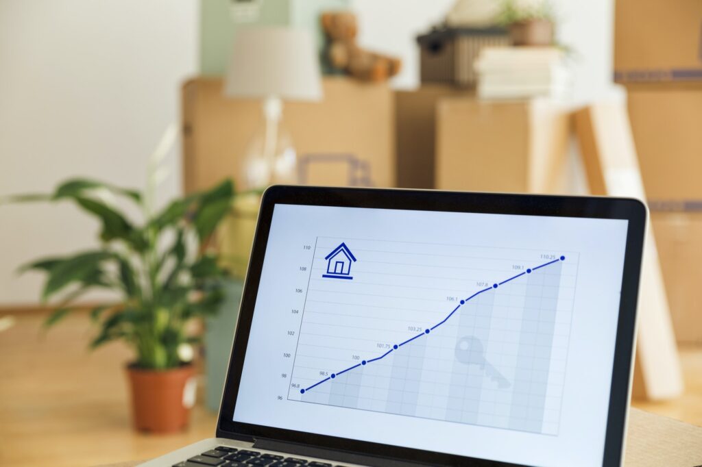 Rising line graph on laptop screen in front of cardboard boxes in a new home