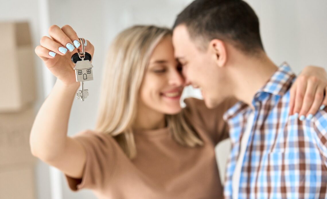 Happy young couple first time home owners holding keys in new home, closeup.