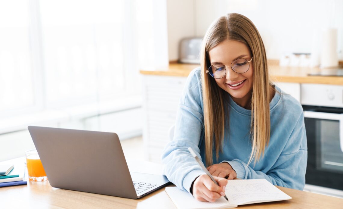 Image of woman making notes in planner while working with laptop