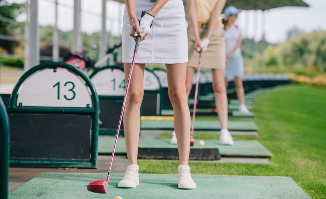 partial view of women with golf clubs playing golf at golf course