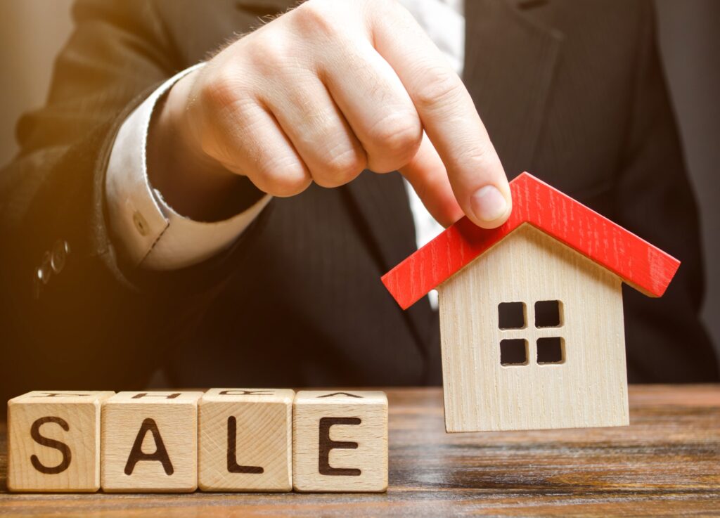 Wooden blocks with the word Sale and miniature house in the hands of a real estate agent