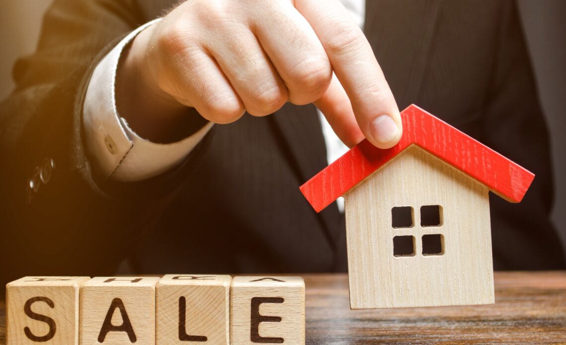 Wooden blocks with the word Sale and miniature house in the hands of a real estate agent