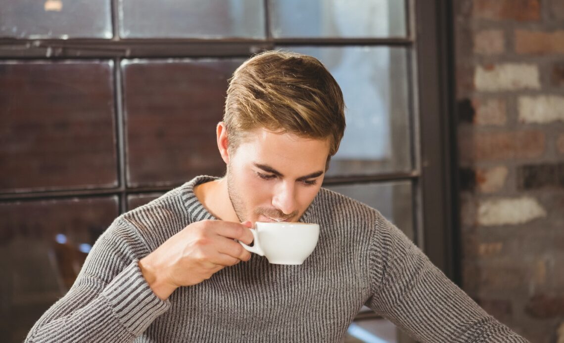 Handsome man drinking coffee and reading newspaper at coffee shop