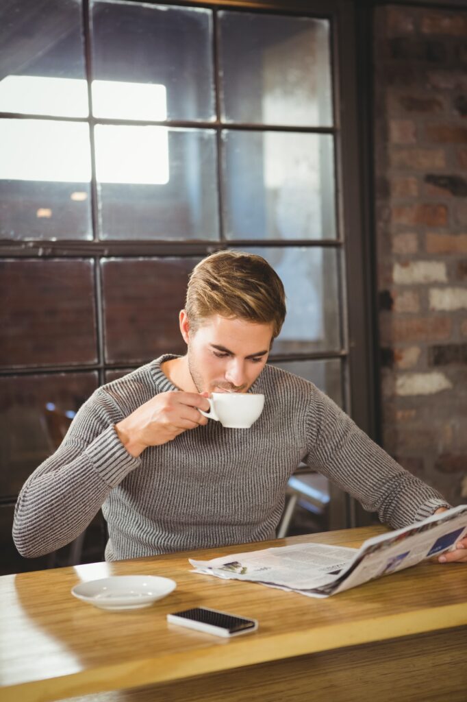 Handsome man drinking coffee and reading newspaper at coffee shop