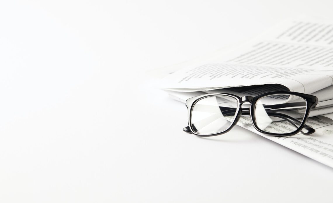 pile of newspapers with eyeglasses, on white background with copy space