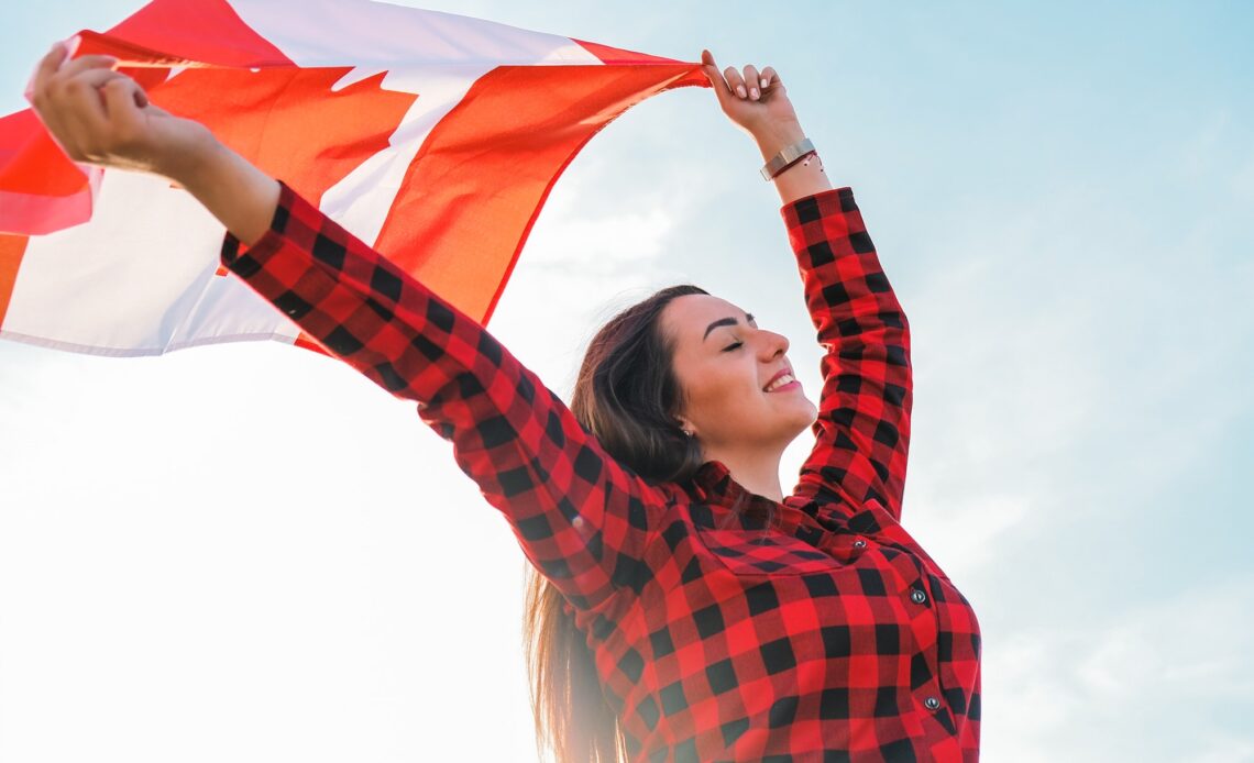 Young millennial brunette woman holding The National Flag of Canada. Canadian Flag or the Maple Leaf