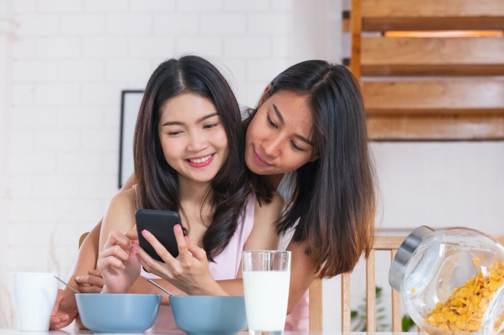 Happy asian lesbian woman couple watching morning news on mobile