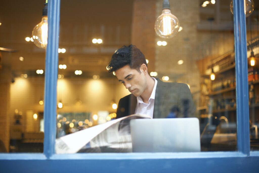 Window view of businessman reading broadsheet news in cafe