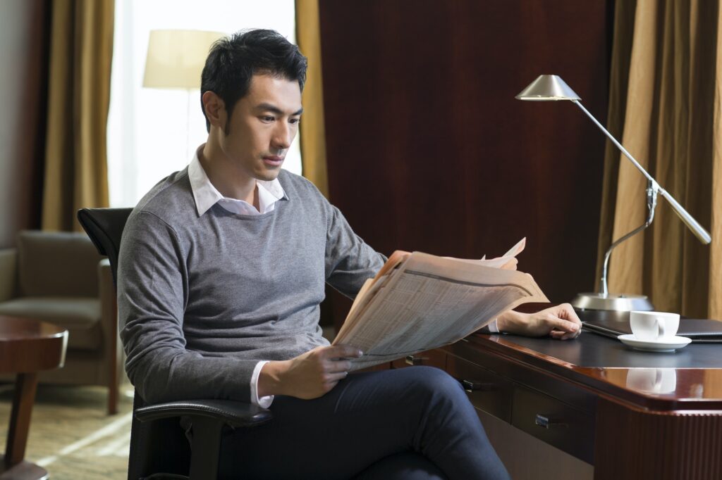 Young businessman reading newspaper in study
