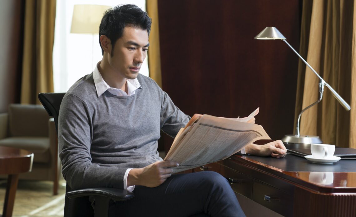 Young businessman reading newspaper in study