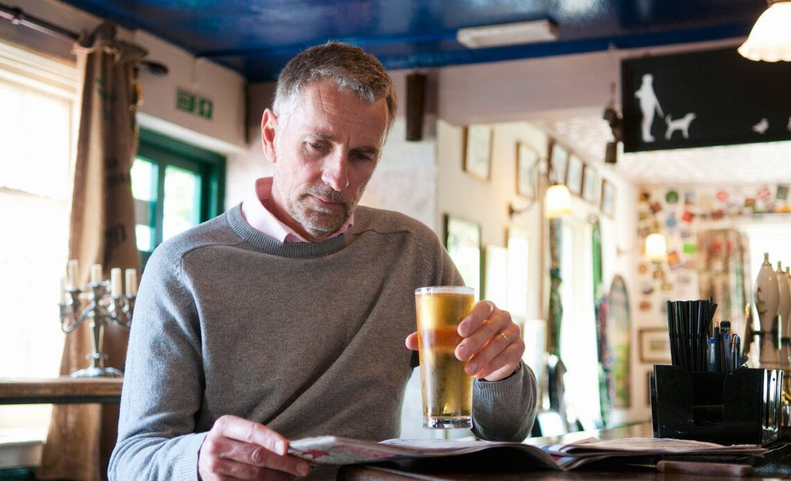 Mature man drinking beer and reading newspaper in pub