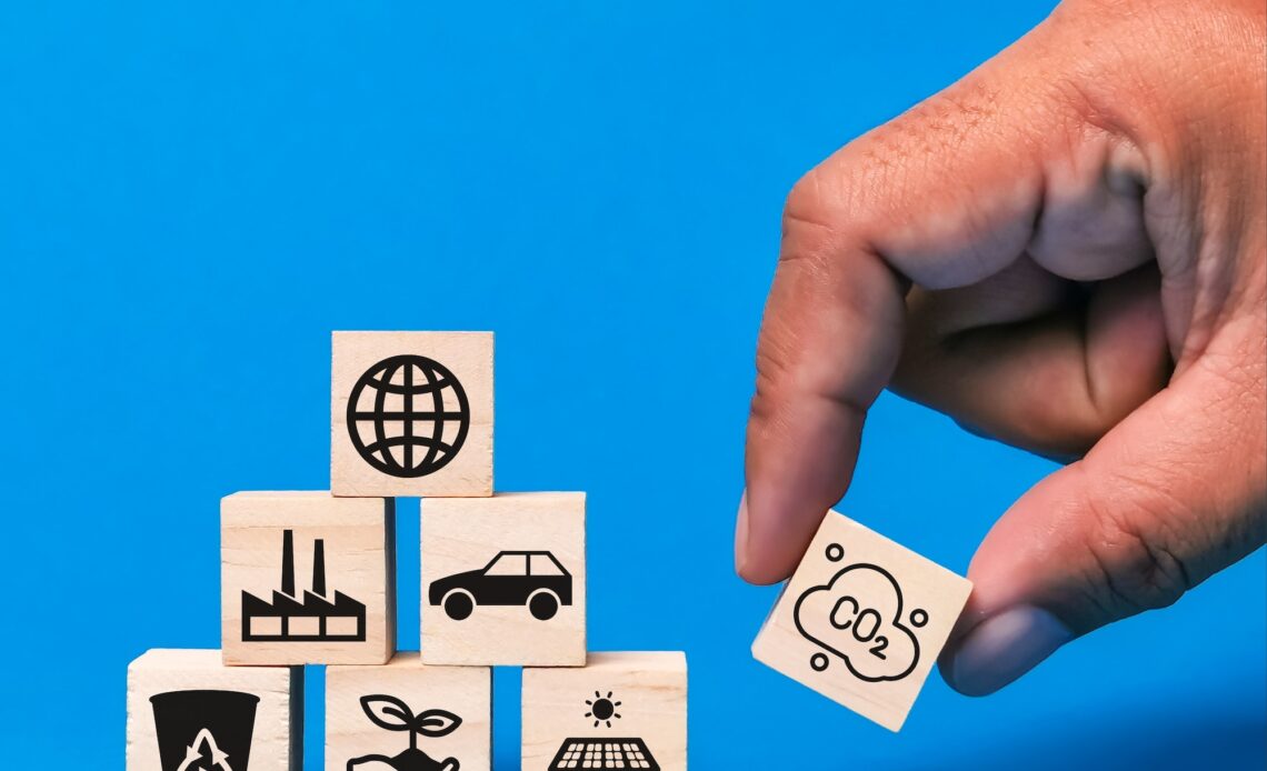 Business and environment concept. Hand putting wooden cube with icons against blue background.