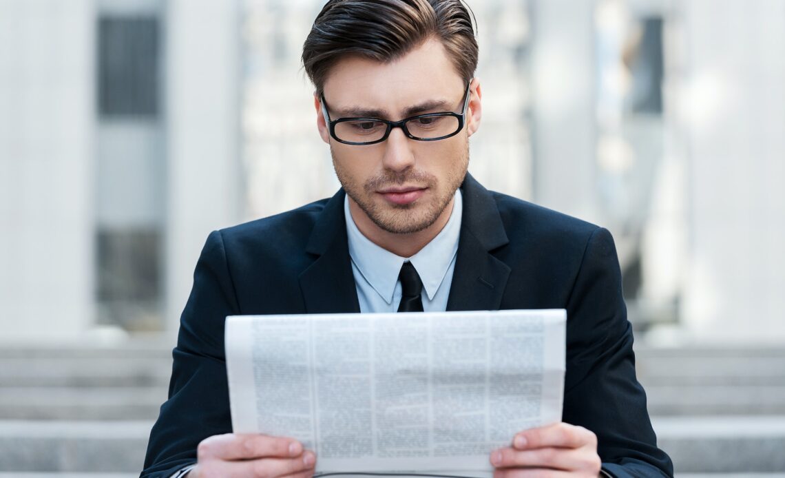Morning news. A young businessman reading a newspaper outdoors