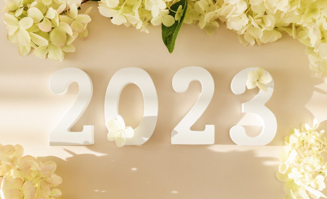 White wooden number 2023 on pastel beige background with flowers. Happy New Year 2023.