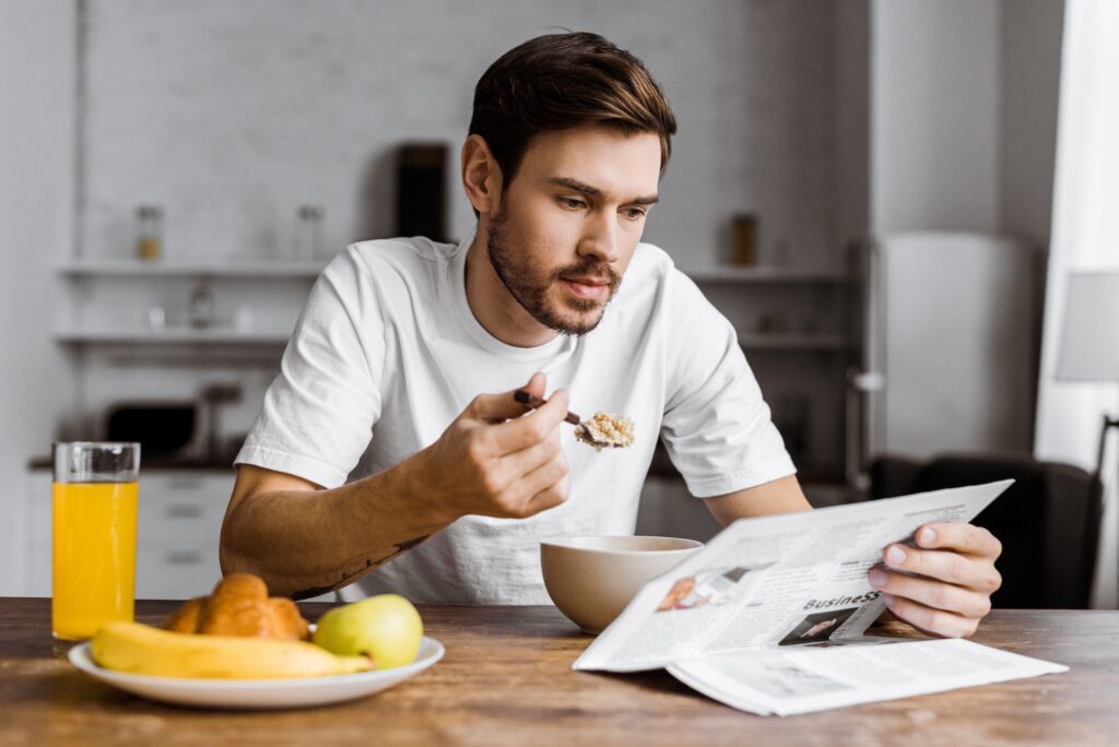 handsome young man having cereal for breakfast and reading newspaper at home