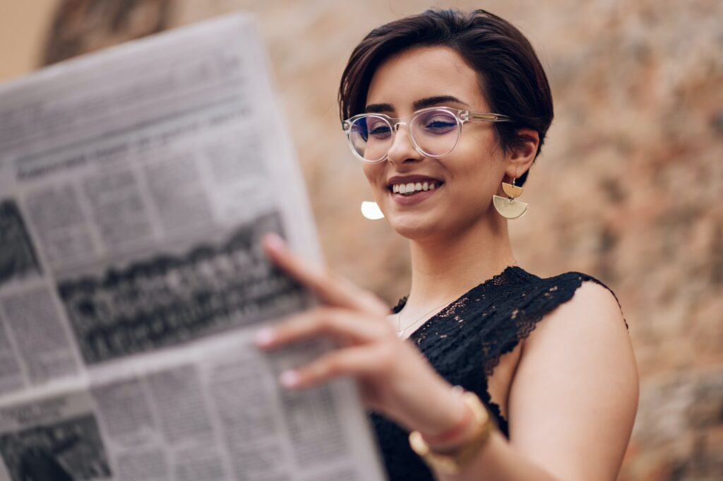Portrait of a woman with eyeglasses reading newspaper outside